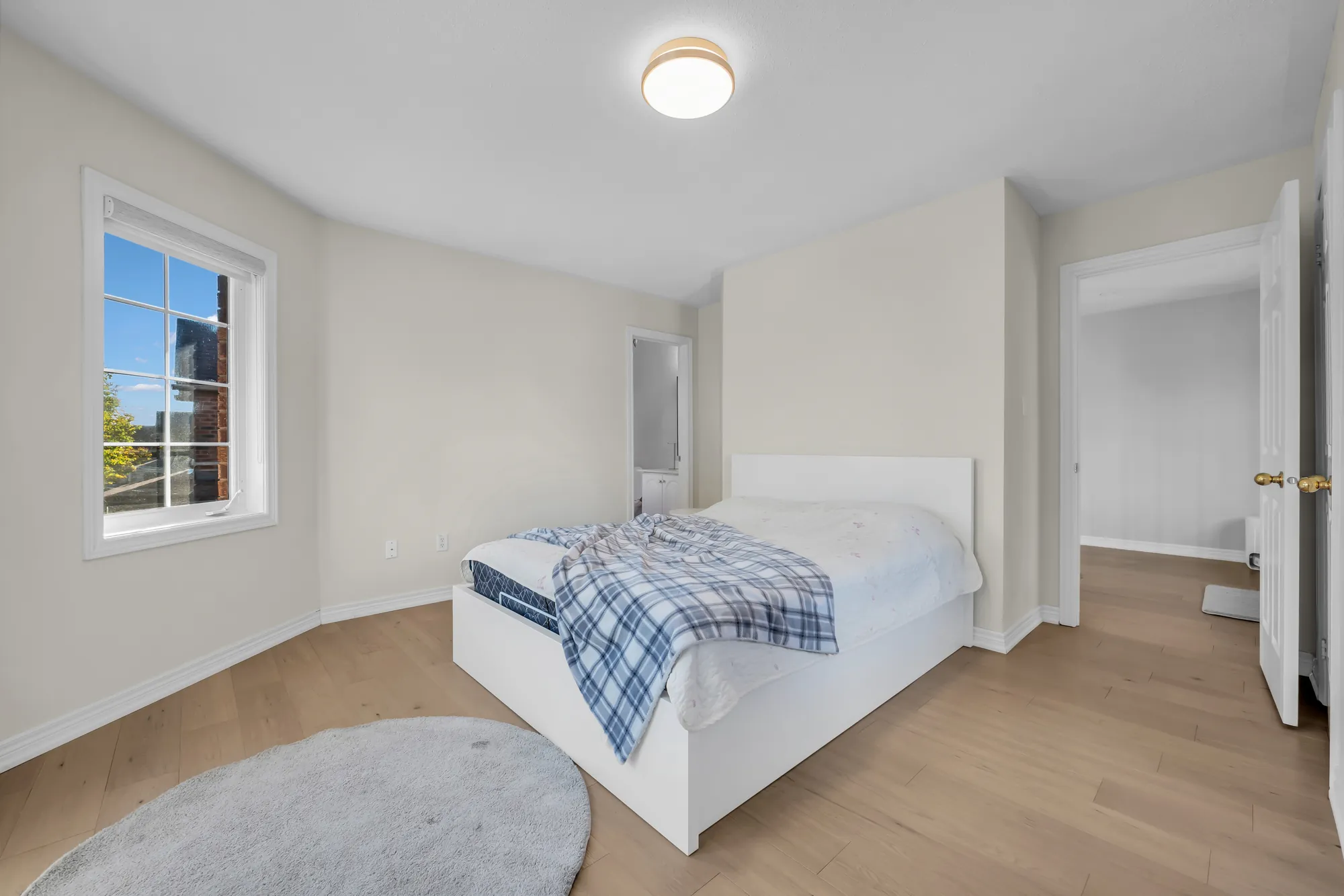 The same bedroom toward its doors, a white bed, a round rug, a doorway open at the right