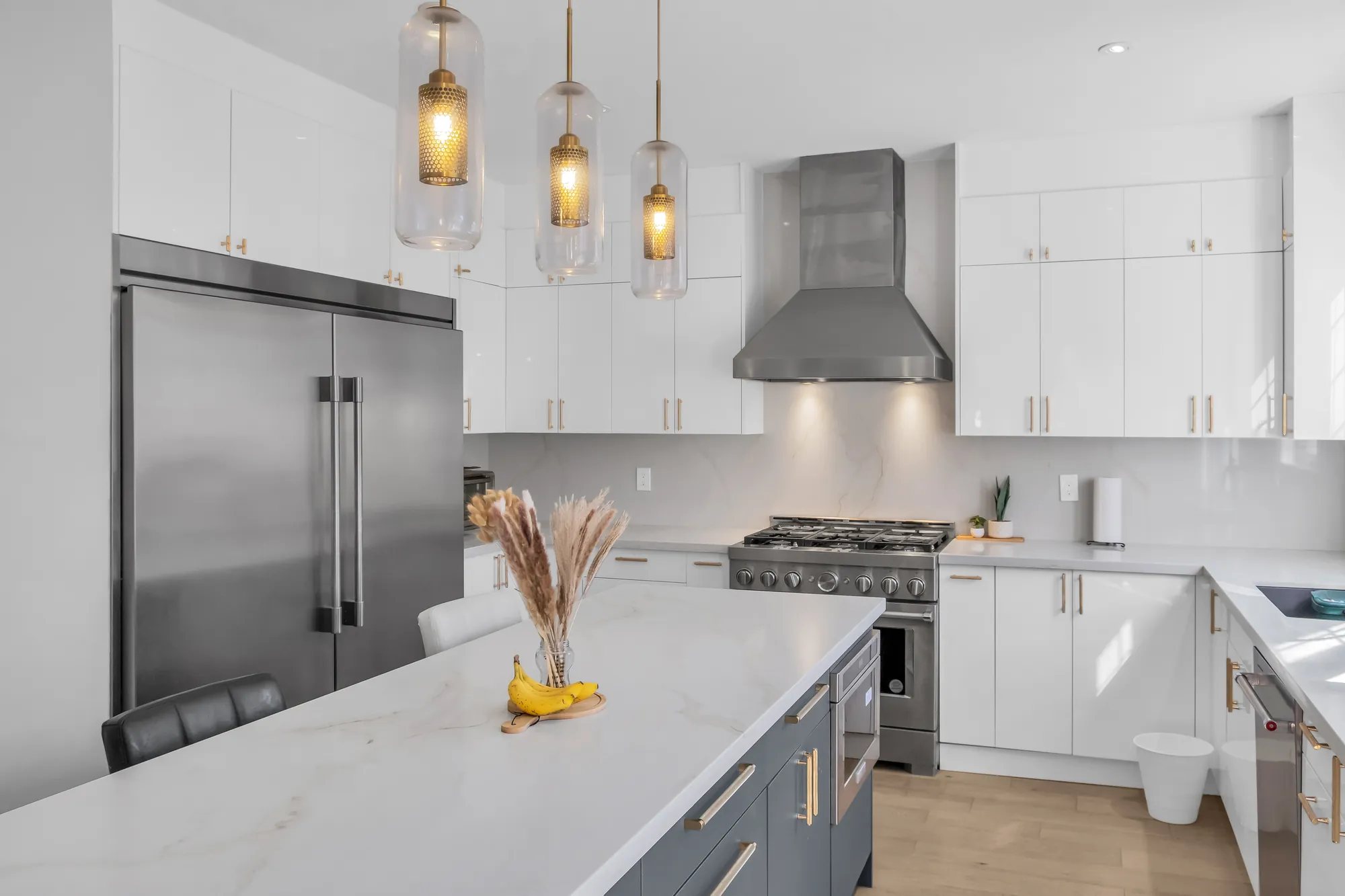 A close view of the island, the built-in fridge, the pendants and the range under the hood