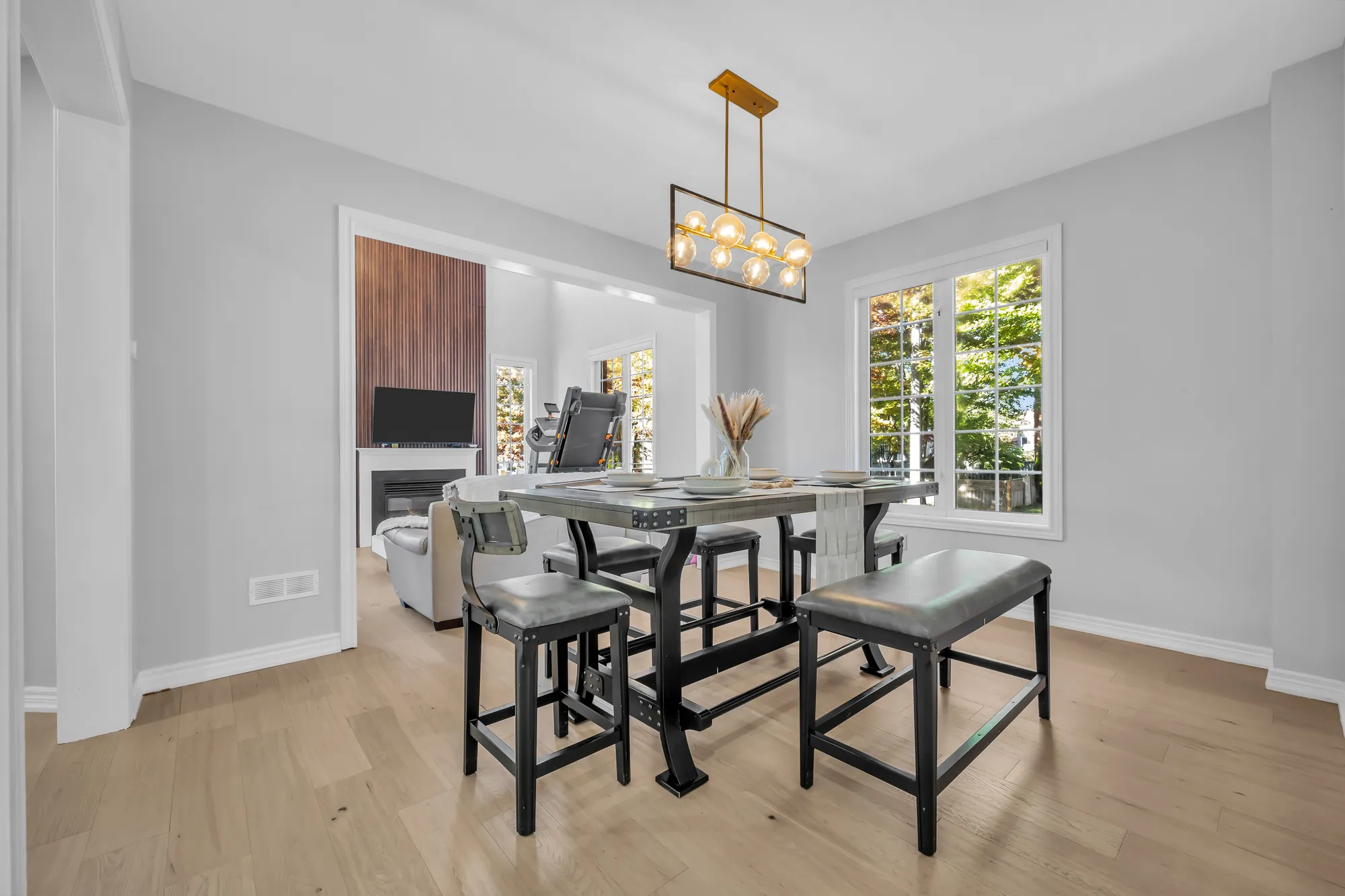 The dining table toward a wide opening to the family room, the fireplace under its wood-slat wall beyond, windows at the right
