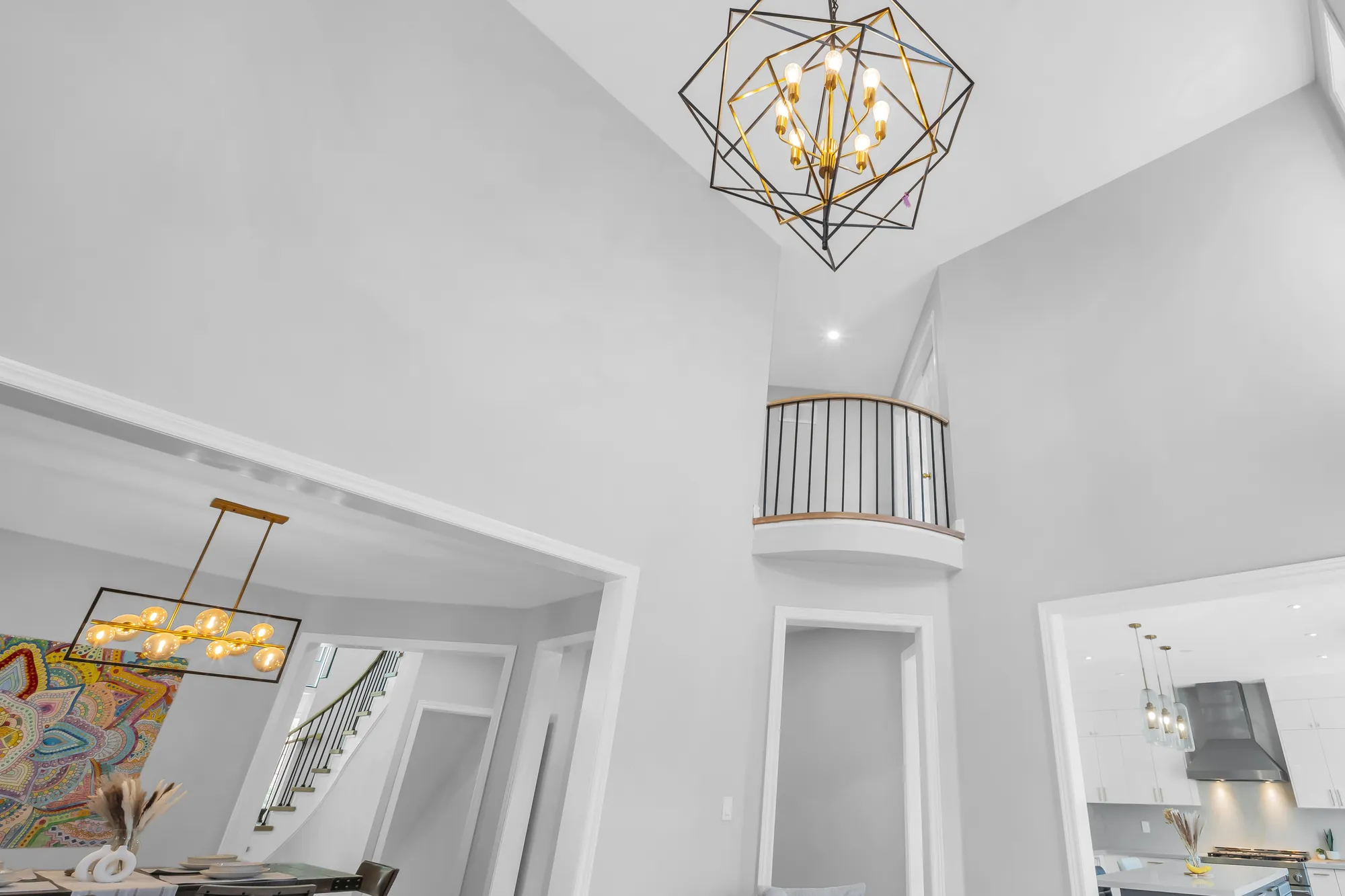 Looking up from the family room: the geometric chandelier, the curved balcony of the upper hall, the dining room and the kitchen through wide openings below