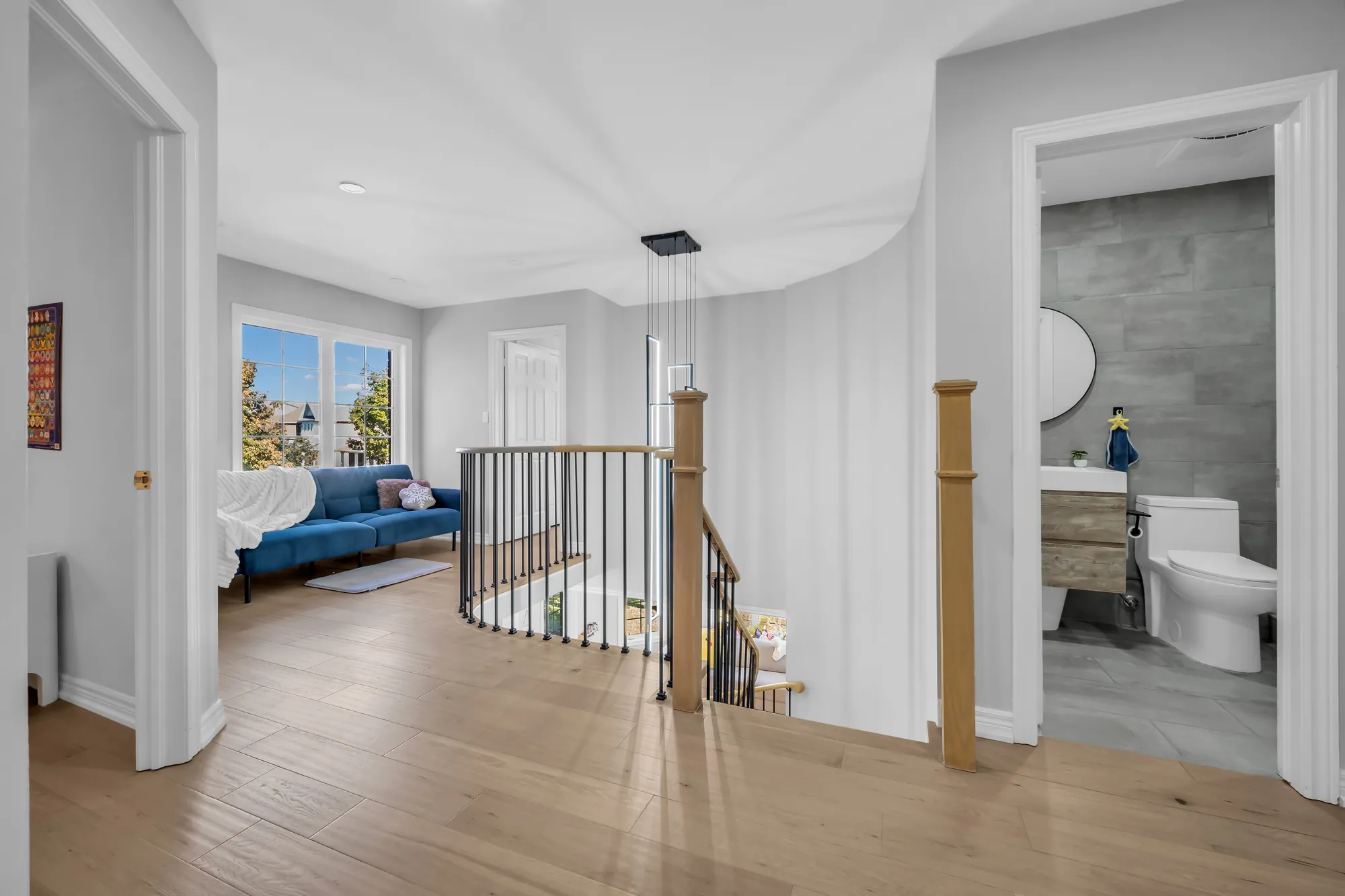 The upper hall: the curved stair railing in oak and black spindles, a loft with a blue sofa under a window at the left, a bathroom through a door at the right