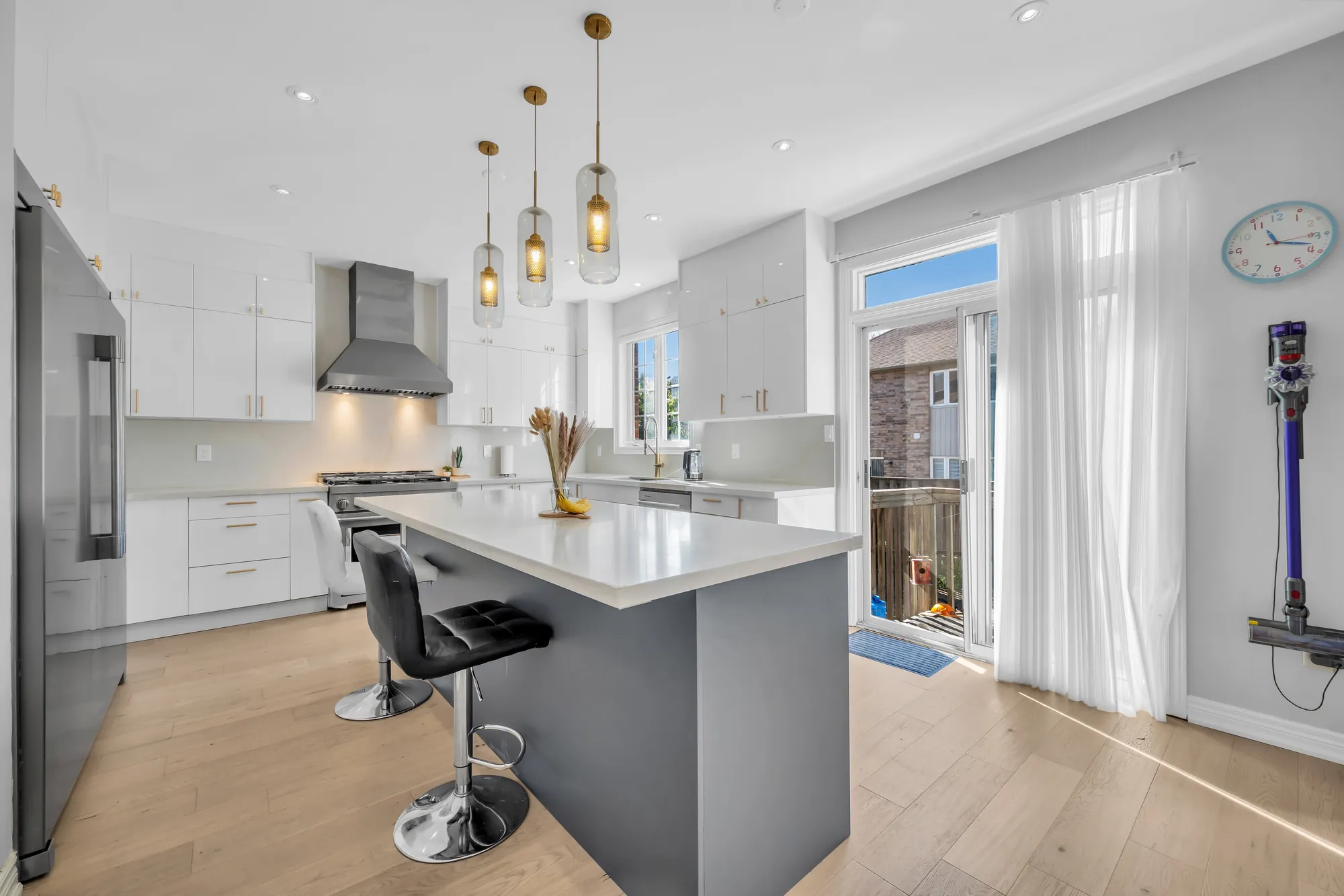 The kitchen toward the door to the back yard: the island with bar stools, white cabinets, the range and hood, a glass door with a sheer curtain