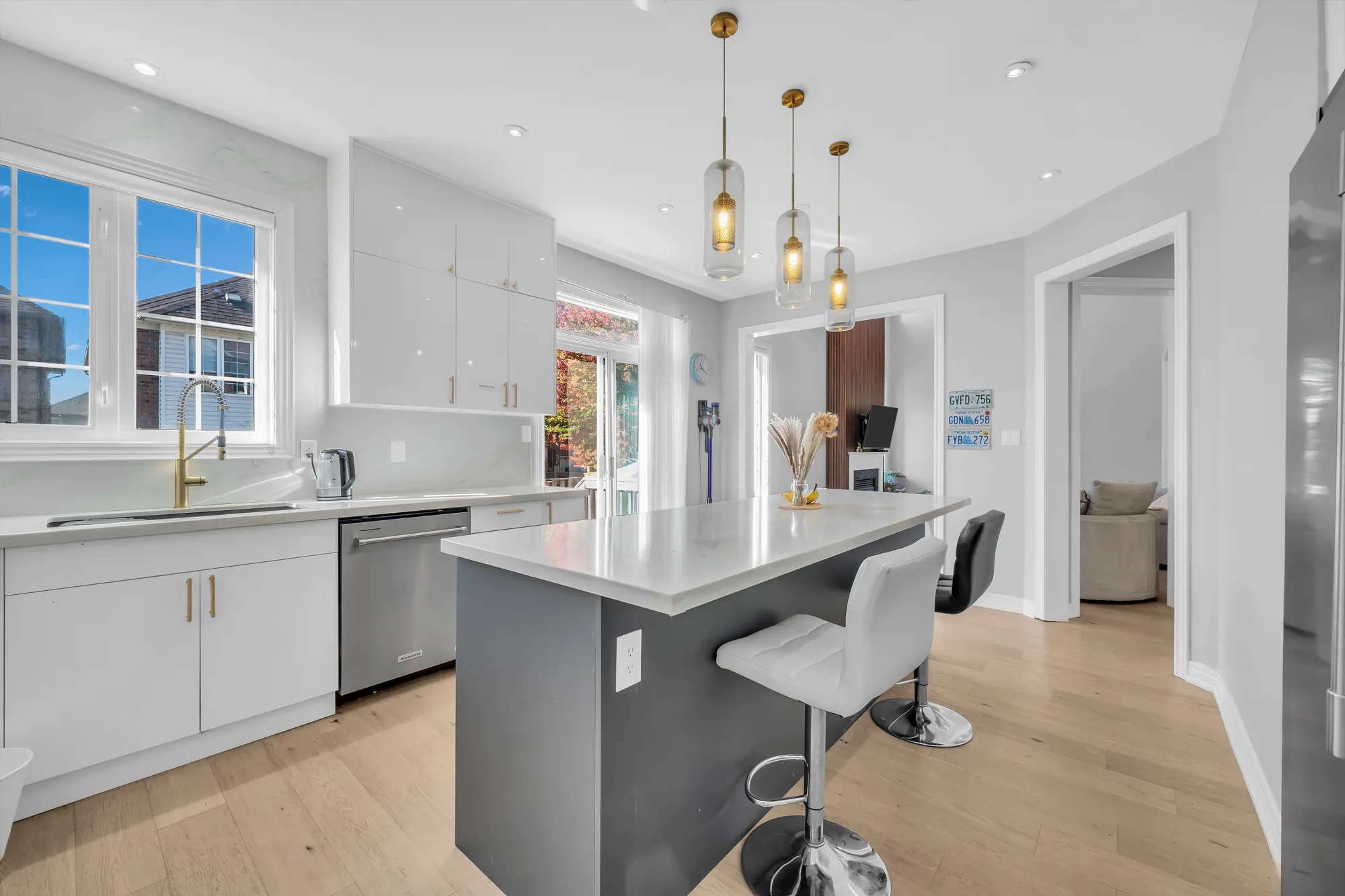 The sink under a window, a dishwasher, the grey island with white bar stools, the family room through the opening at the right