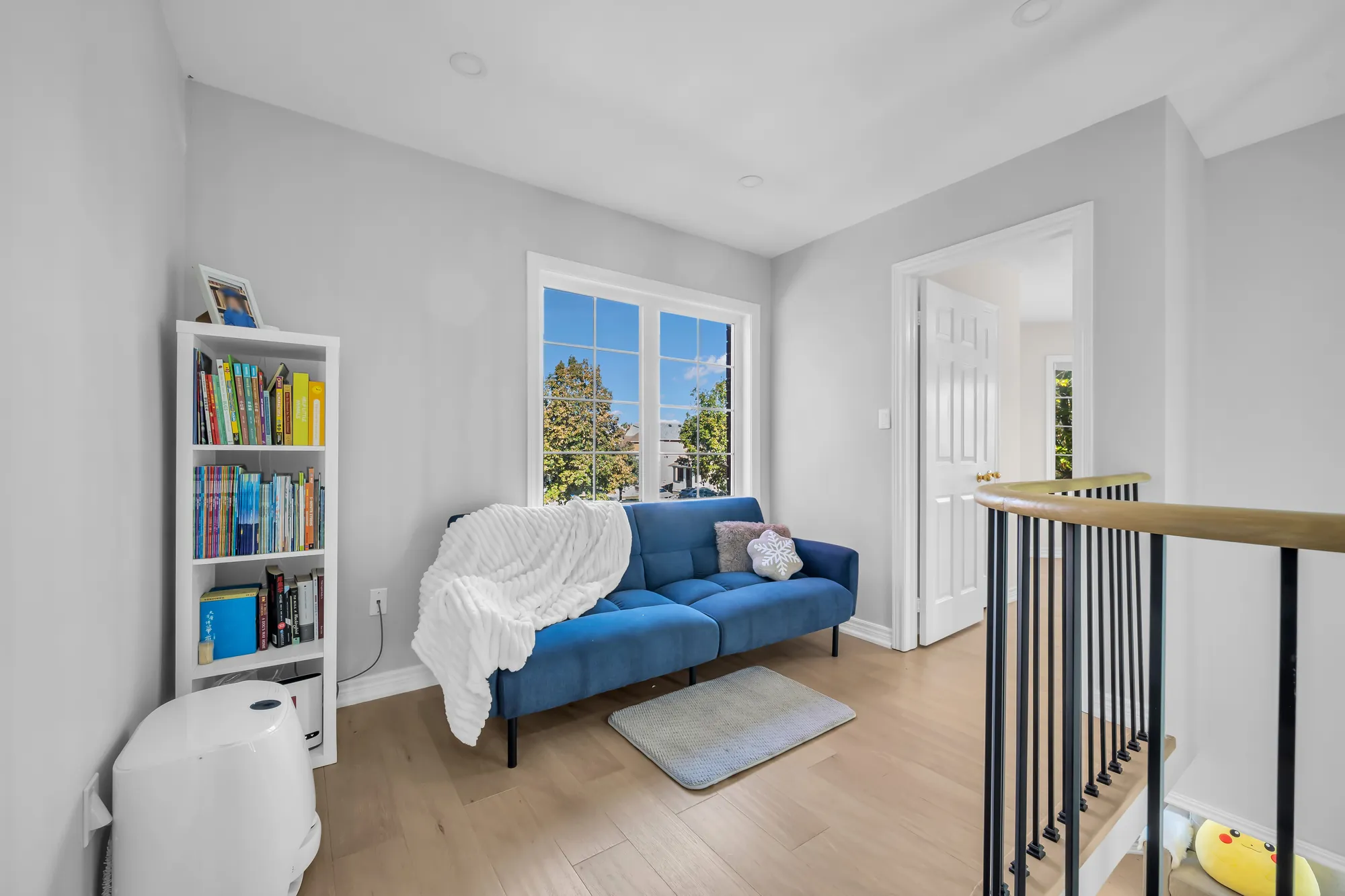 The loft beside the stairwell: a blue sofa under a window, a bookcase, the oak and black railing at the right