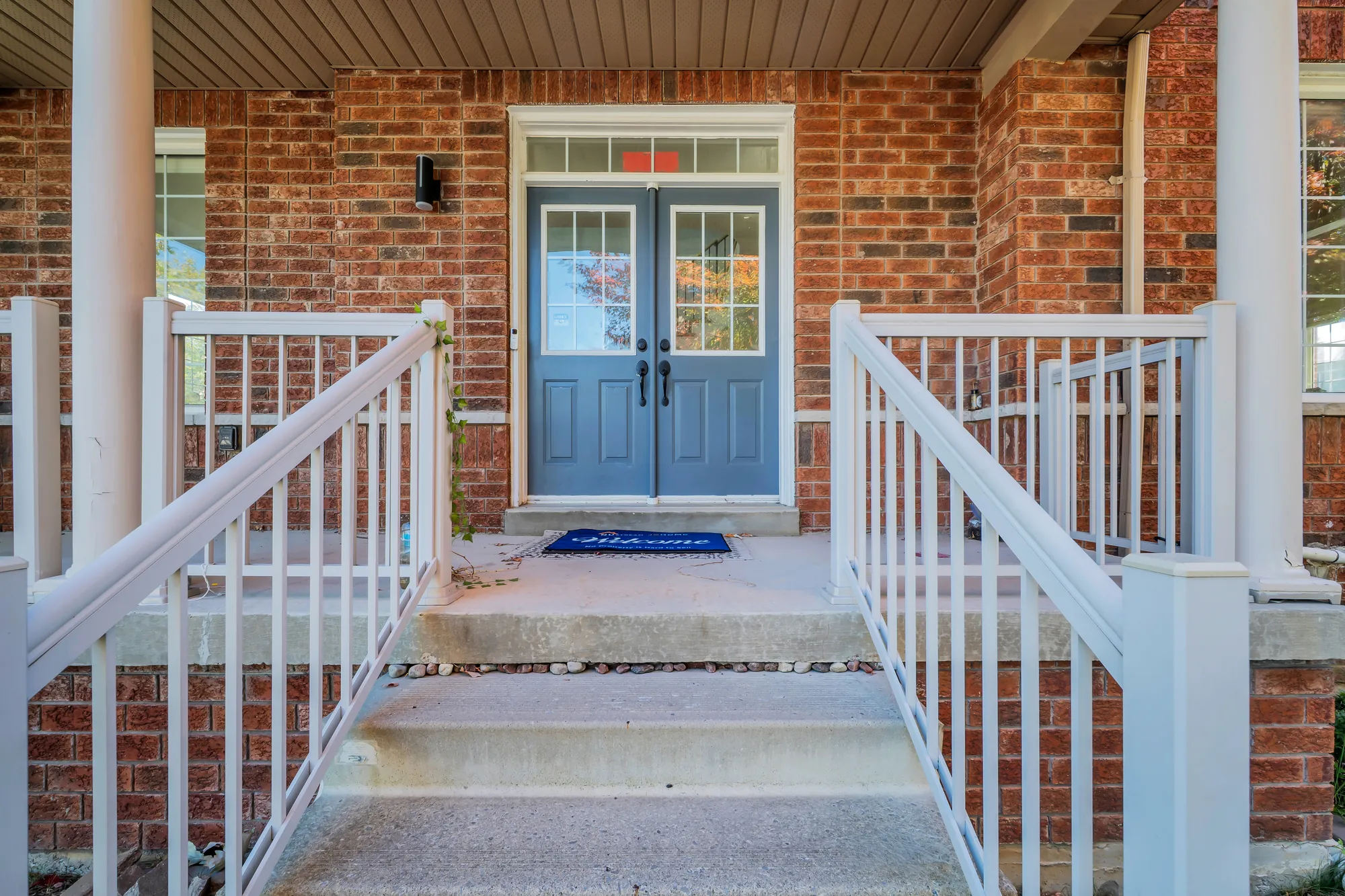 The front door: a pair of blue doors with glass panels under a transom, red brick, white columns and railings, concrete steps up to the porch