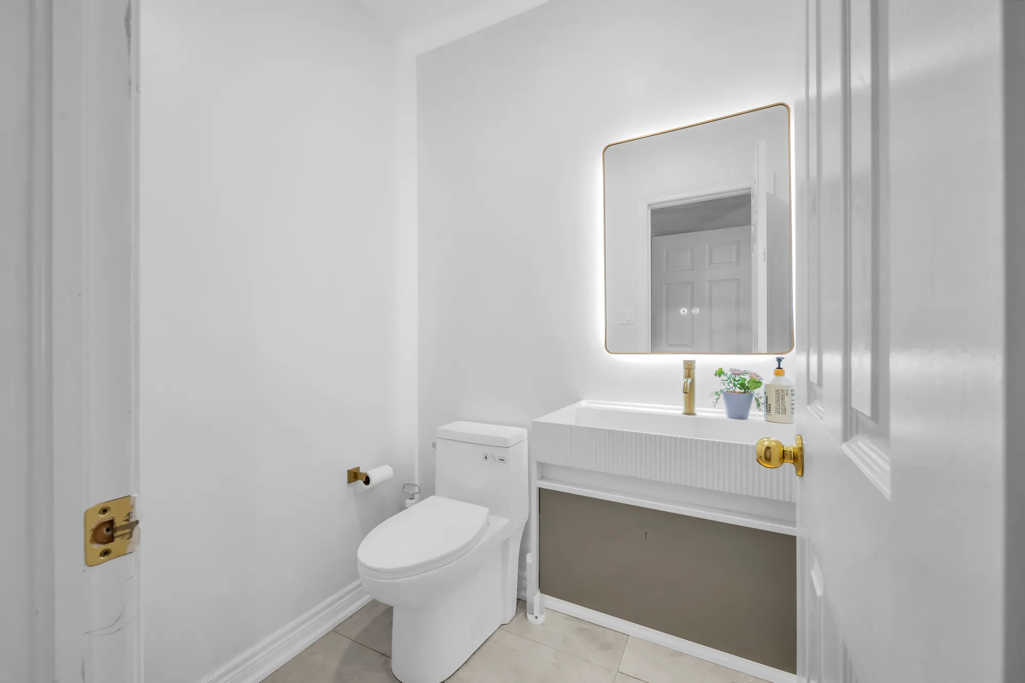 The powder room: a toilet, a white wall-hung vanity, a backlit mirror, brass fittings