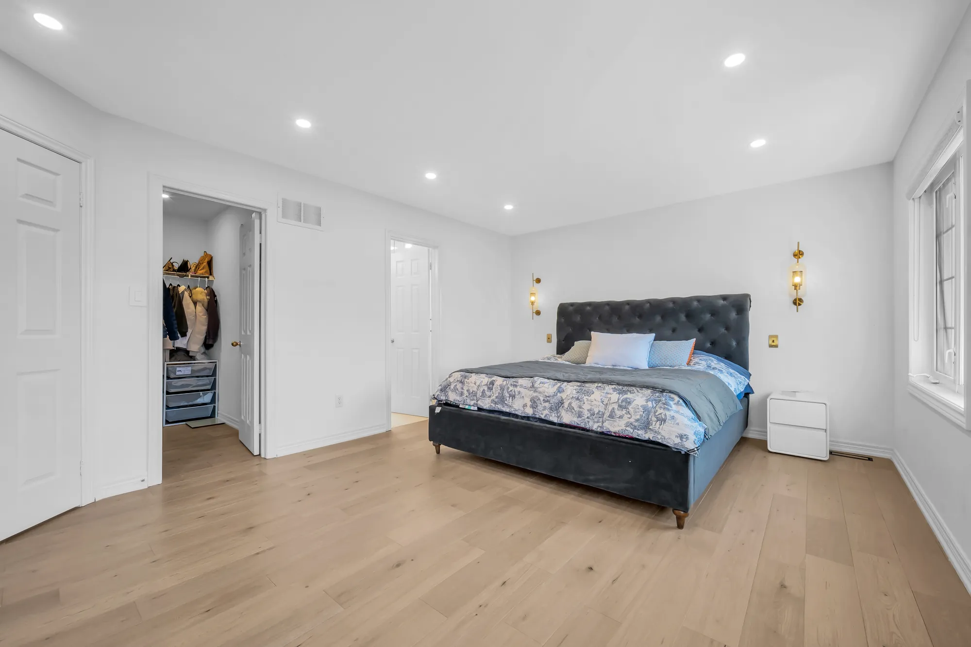 The primary bedroom toward the doors to the walk-in closet and the bathroom, the bed and a white night table at the right