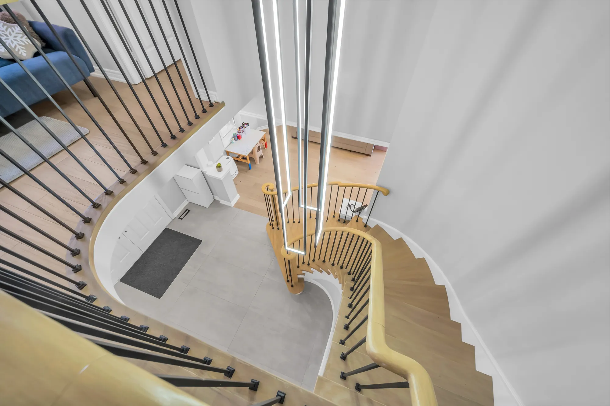 Looking down the curved staircase into the foyer from the upper floor, a long linear light hanging through the stairwell