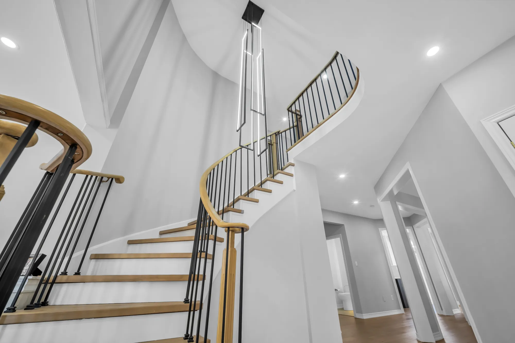 The curved staircase from below, oak treads and handrail, black spindles, the upper hall above